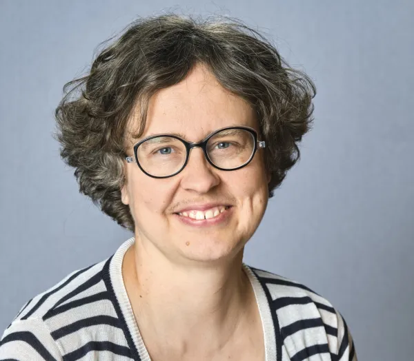 Olesya Khanina. Olesya Khanina wearing glasses and a striped shirt, smiling at the camera.