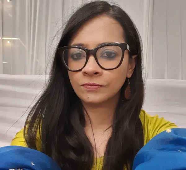 A woman wearing glasses, with a long, dark hair, looking solemnly into the camera
