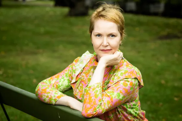 Astrid Joutseno sits on a park bench, head resting on hand, in a colorful shirt.