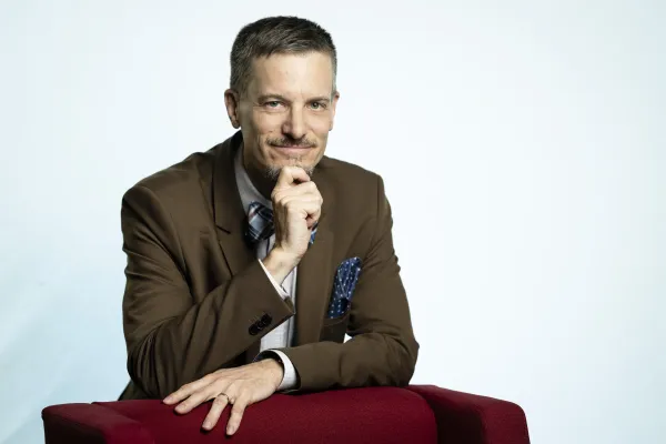 Carl Johan leaning against a red chair with his hand on his chin.