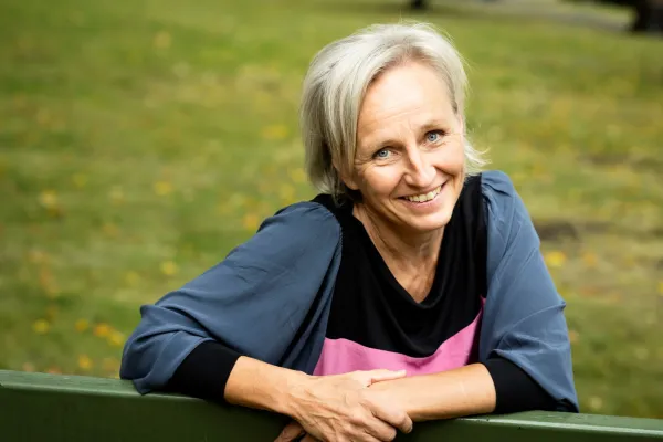 Elina Oinas sitting on a park bench, smiling widely.