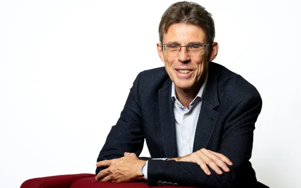 Christian leaning against a red chair and smiling.
