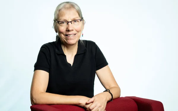 Anne leaning against a red chair and smiling.