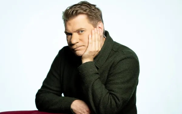 Timo leaning against a chair and resting his hand on his face.