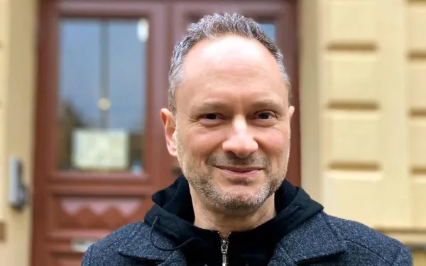 Fred Markowitz. Fred Markowitz standing in front of a yellow building, smiling softly.