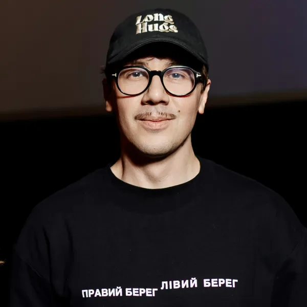 Headshot of Andriy wearing a black cap that says “Long Hugs” and a black T-shirt with Cyrillic text.