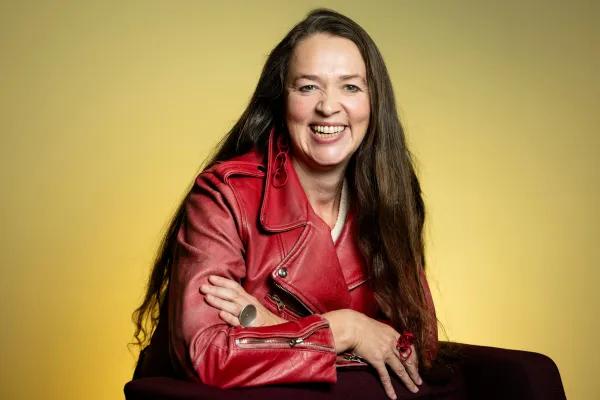 Kristina Jacobsen. Photo by V. Somerpuro. Kristina Jacobsen wearing a red leather jacket, leaning against a chair and laughing.
