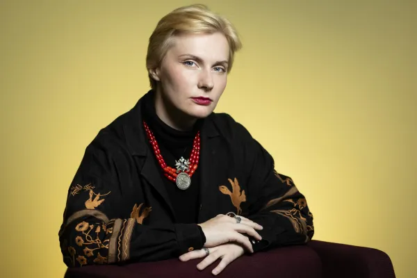 Tetiana Kalytenko. Photo by V. Somerpuro. Tetiana Kalytenko, wearing a black jacket with brown patterned sleeves and a red beaded necklace with a large pendant, hands resting on the arm of a chair.