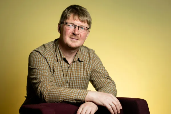 Mihail Kopotev. Photo by V. Somerpuro. Mihail Kopotev wearing glasses and a button-up shirt, leaning against the back of a chair.