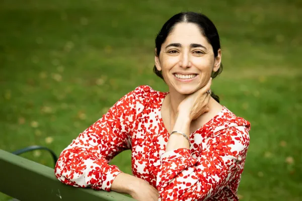 Nicole Hassoun in a red floral shirt, resting her hand against her neck and smiling widely.