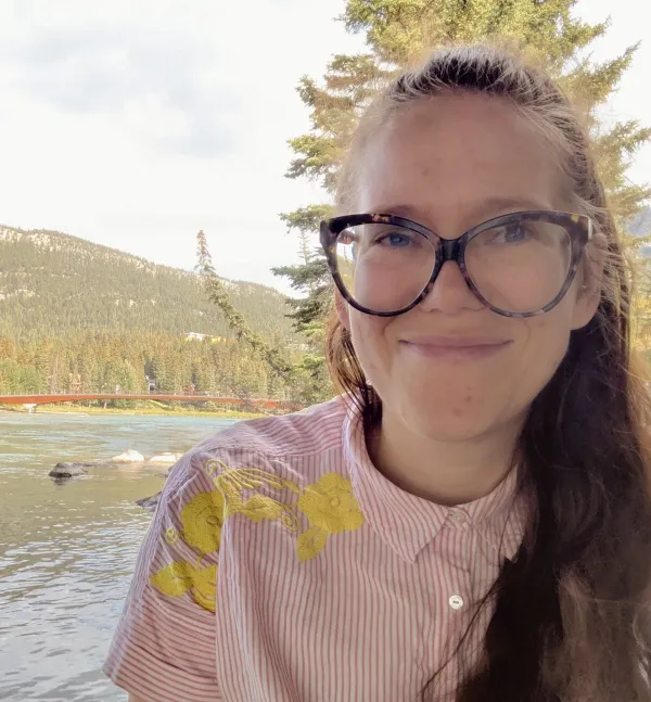 Serrin smiling outside. In the background there's a body of water and a mountain.