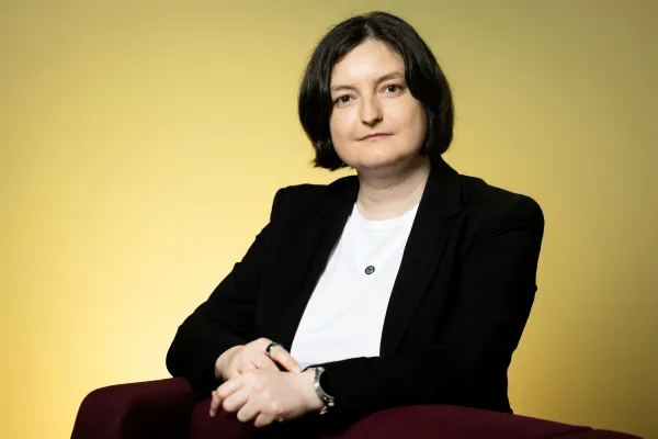 Jitka Štollová wearing a black blazer and white shirt, arms crossed on the back of a chair.