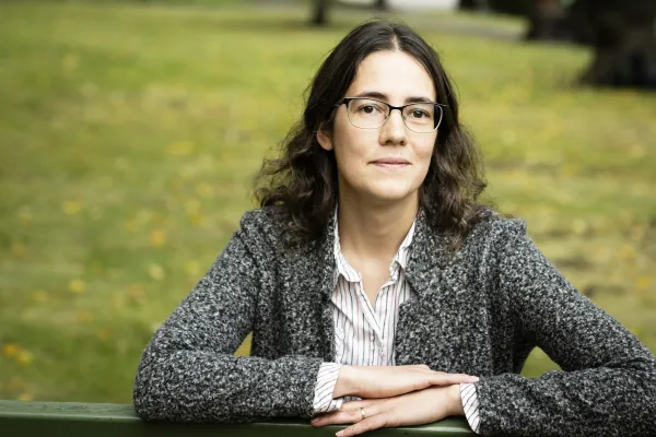 Tatiana Kachkovskaia seated on a park bench, arms resting on the backrest, wearing eyeglasses, button-up shirt, and cardigan.