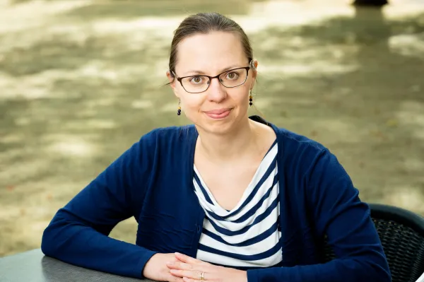Katja Kujanpää. Photo by V. Somerpuro. Katja Kujanpää sitting at a table with her arms crossed on the tabletop.