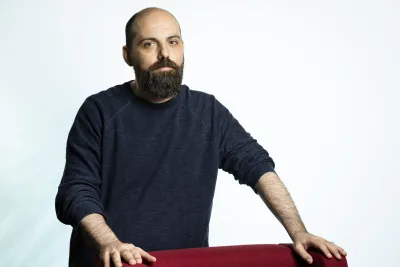 Paolo standing while holding onto a red armchair.