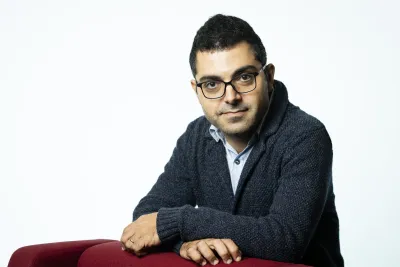 Uğur leaning against a red chair.