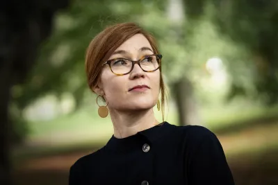 Amanda Lagerkvist wearing glasses, large earrings, and a black shirt, looking into the distance.