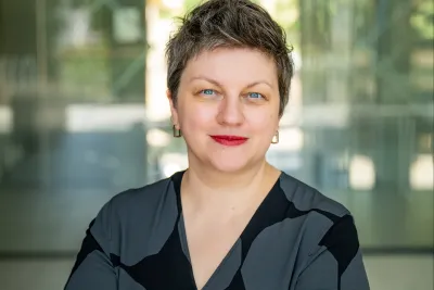 Portrait of Milda Ališauskienė, standing with arms crossed, smiling.