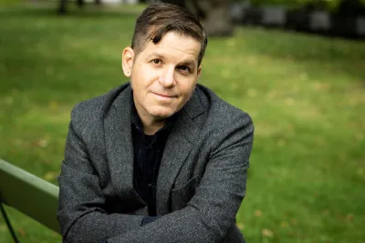 Andrew Graan sitting arms crossed, wearing a gray blazer.