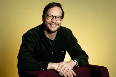 Olle Blomberg wearing a dark green button up and eyeglasses, smiling widely.