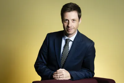Rob Boddice wearing a blue suit, leaning against a chair and smiling.
