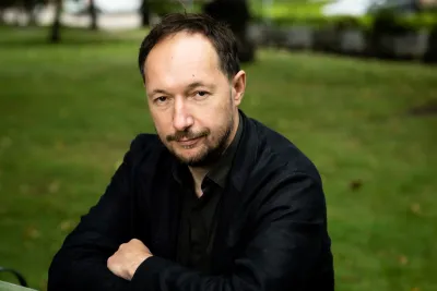 Danila Raskov seated, arms crossed, wearing a black button-up shirt.