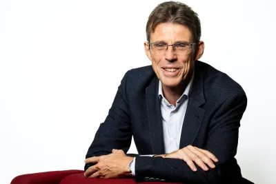 Christian leaning against a red chair and smiling.