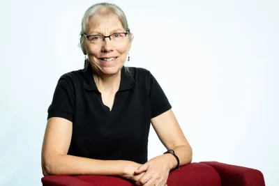 Anne leaning against a red chair and smiling.
