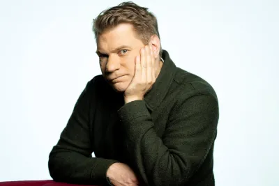 Timo leaning against a chair and resting his hand on his face.