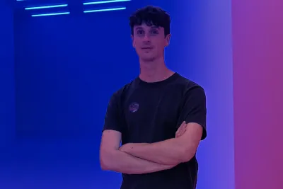Mark standing in a dimly lit room with blue walls. His arms are crossed.
