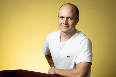 Roope Kaaronen smiling with one hand on his hip and the other resting on the back of a chair.