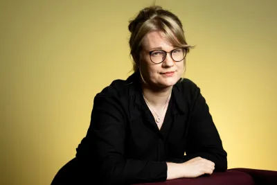Annastiina Kallius wearing glasses and a black outfit, leaning against a chair.