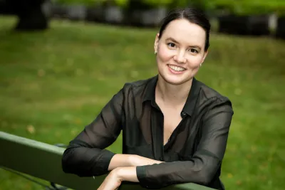 Kateryna Golovina seated on a park bench, arms resting on the backrest, wearing a black button-up shirt.