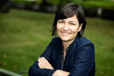 seated on a park bench, arms resting on the backrest, smiling widely.