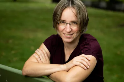 Lina Klymenko sitting on a park bench arms crossed, smiling.