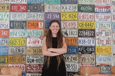 Ksenia Medvedeva standing in front of a wall made of U.S. license plates, arms crossed and smiling broadly.