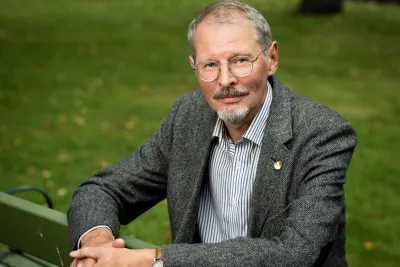 Oleksiy Tolochko in eyeglasses and gray blazer, sitting on a park bench.