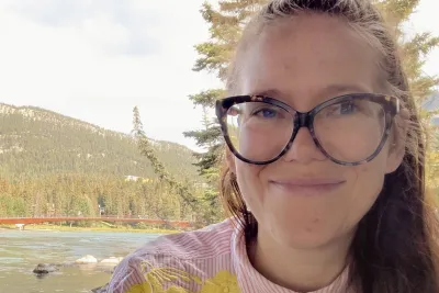 Serrin smiling outside. In the background there's a body of water and a mountain.