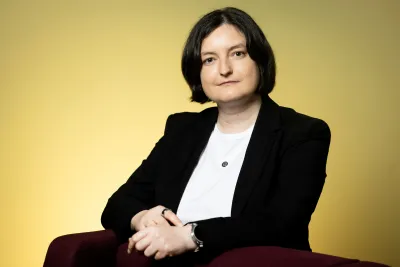 Jitka Štollová wearing a black blazer and white shirt, arms crossed on the back of a chair.