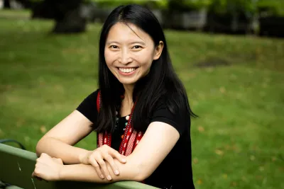 Wasiq Silan seated on a park bench, arms resting on the backrest, smiling widely.